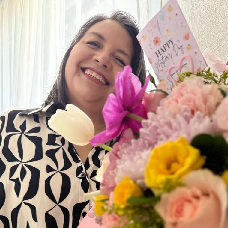 Claudia, creadora de Arte de Claudia, sonriendo junto a un arreglo de flores